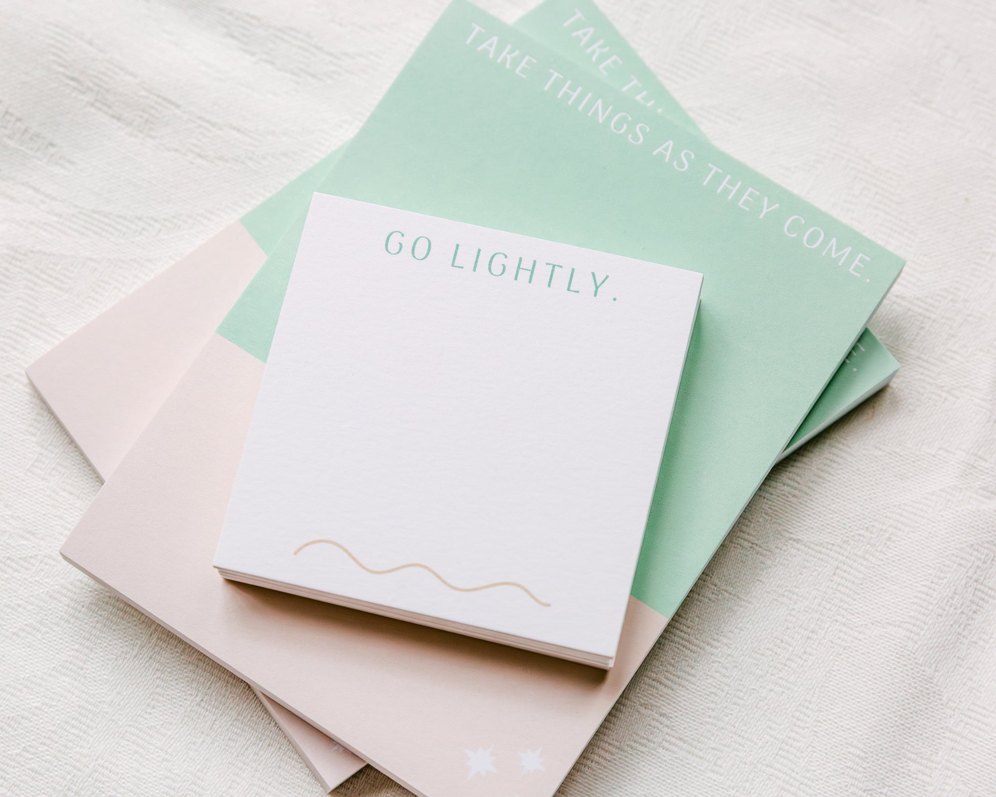 Magpie x Mamey “Go Lightly” post-it pads stacked on matching notepad, styled on fabric background